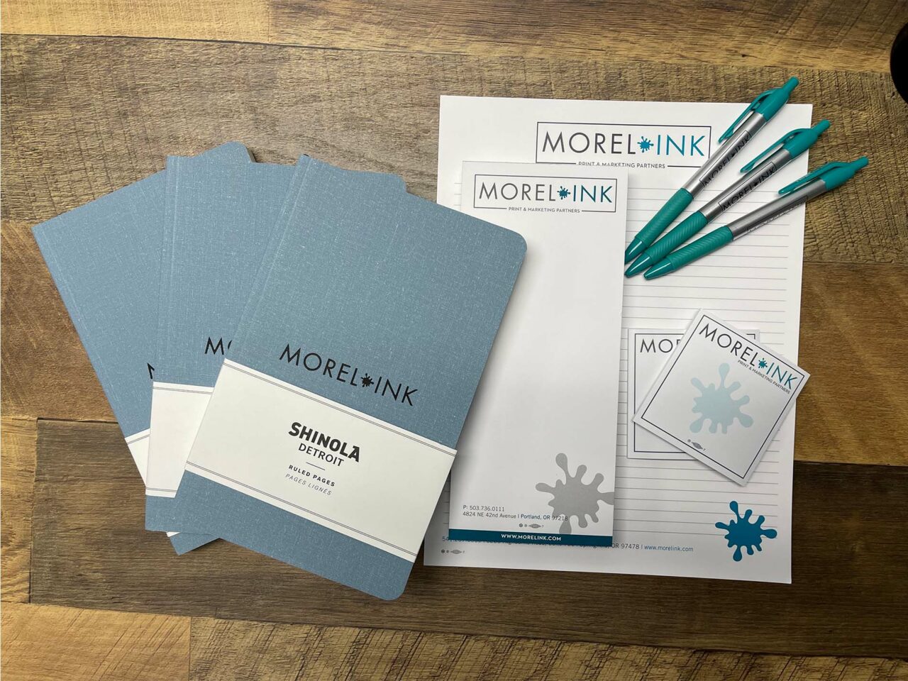 Example of Morel's print and promotional capabilities, showing branded pens, notebooks, notepads, and stickies.
