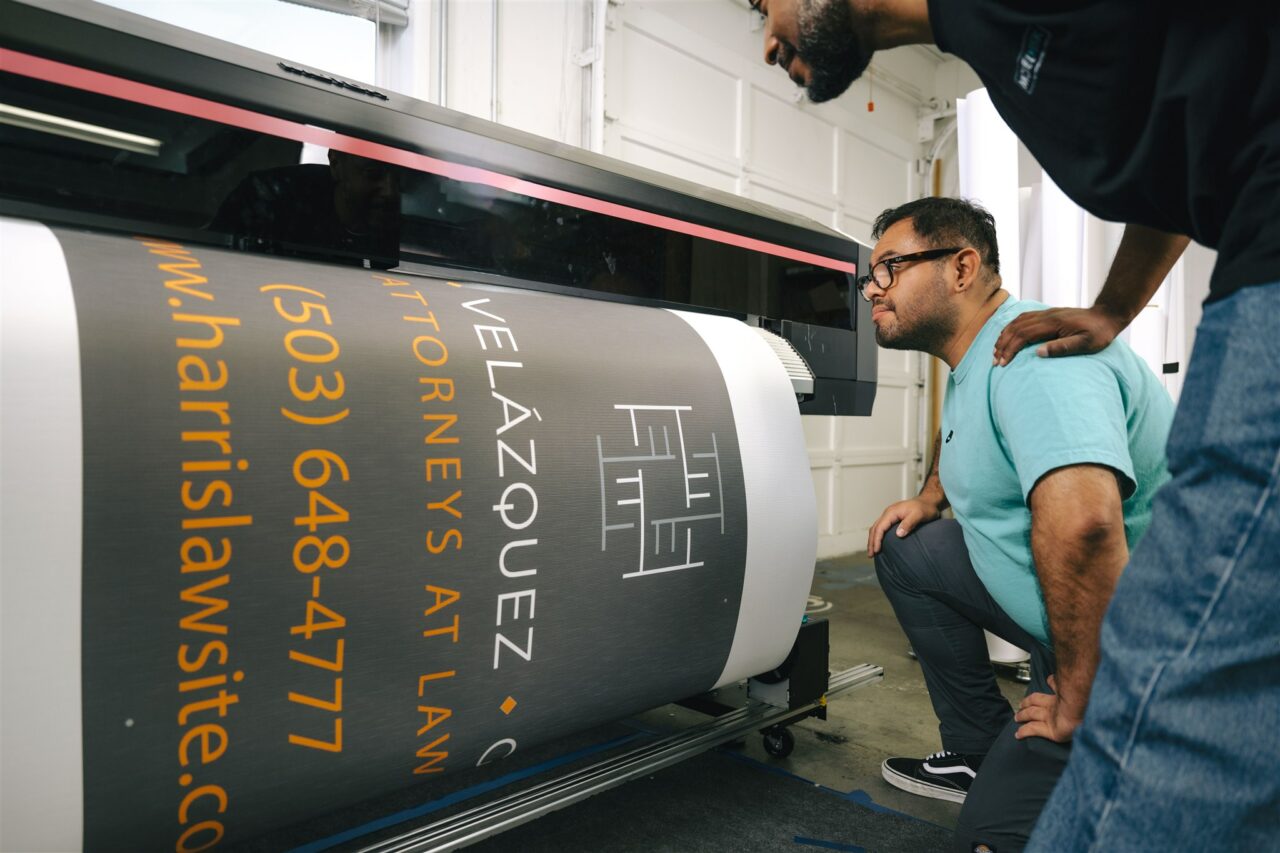 Two Morel Ink team members showcase their wide format printing capabilities with a large banner