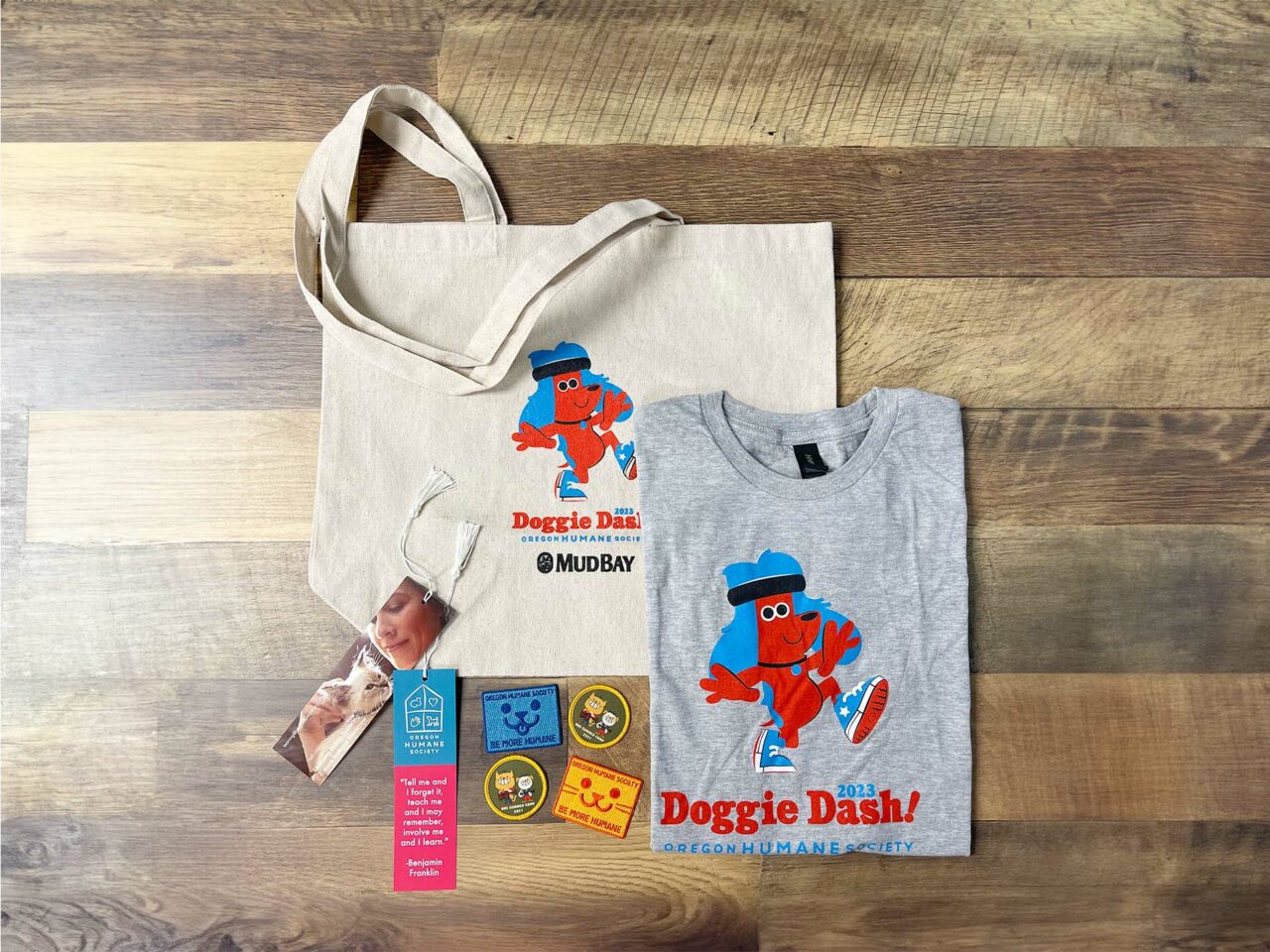Example of Morel's promotional and apparel capabilities, showing a branded tote bag, t-shirt, bookmarks, and embroidered patches for the Doggie Dash.